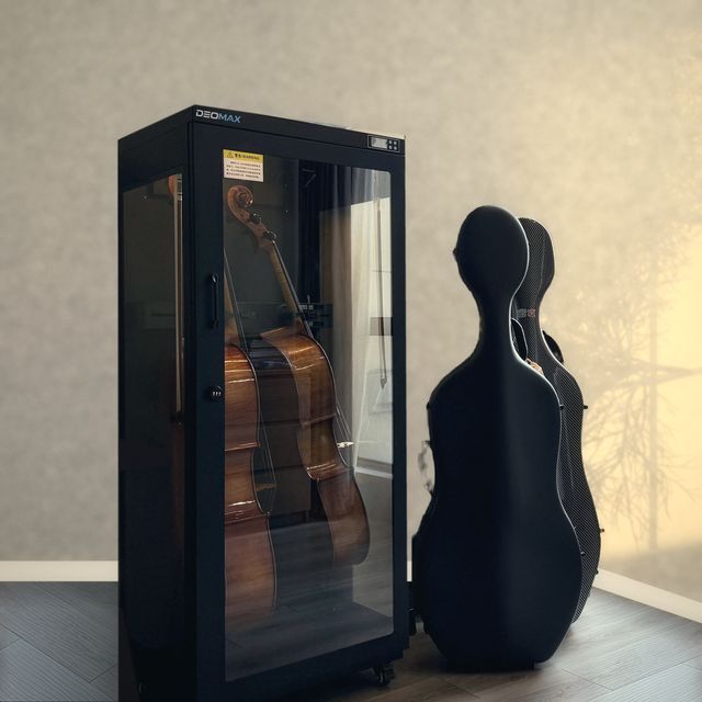 Two cellos stored in a DEOMAX cabinet beside carbon cello cases